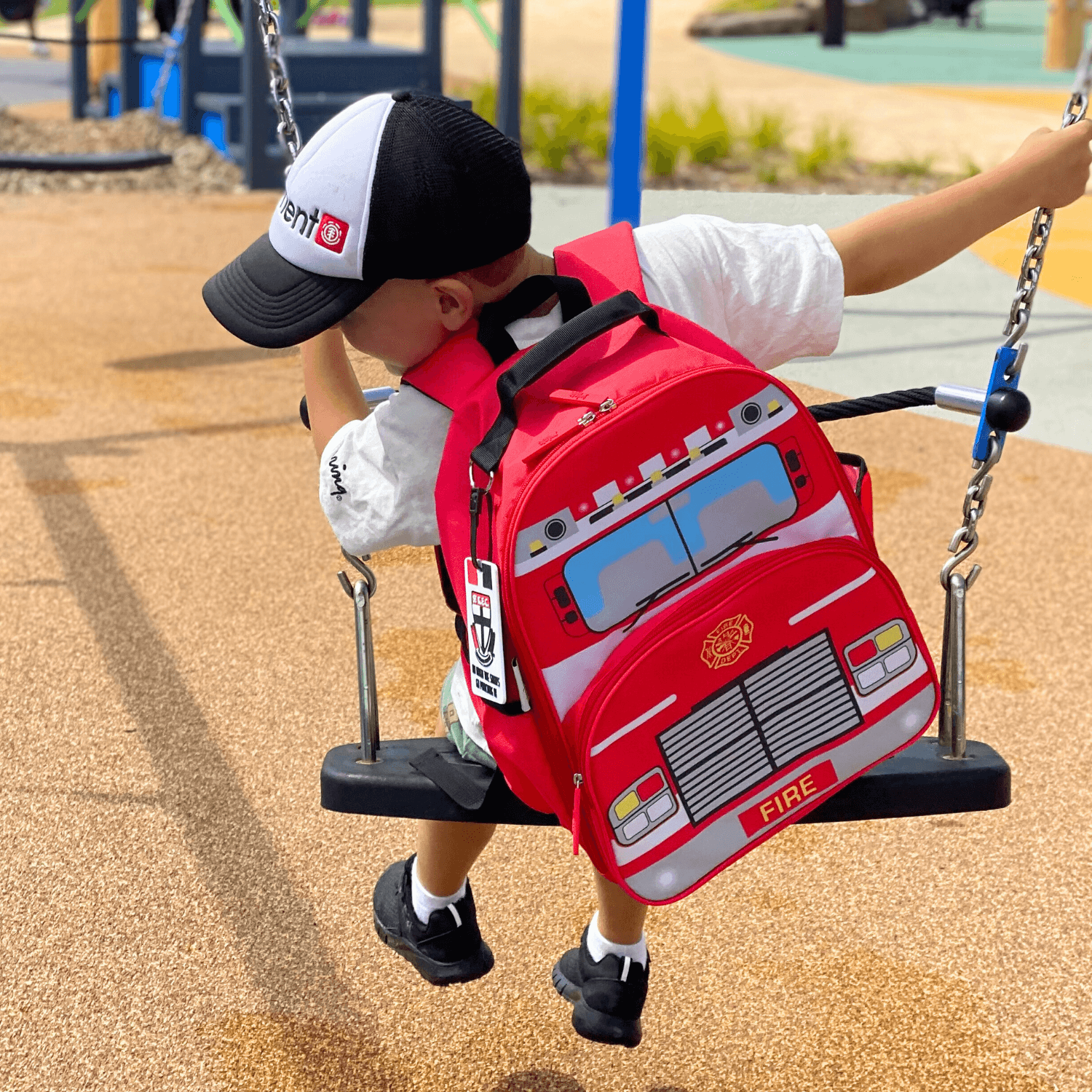 Boy swinging on swing wearing jude&moo Boys Fire Truck Backpack