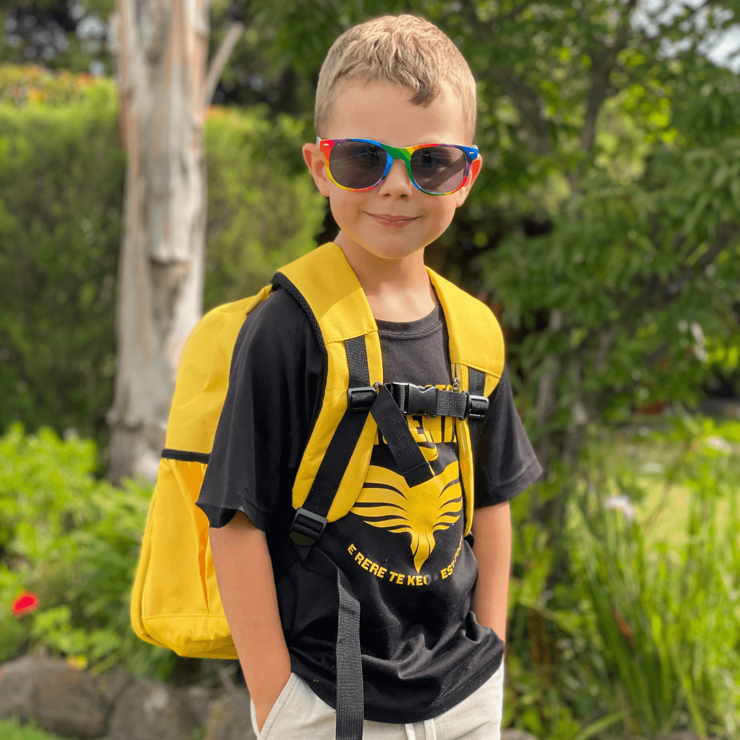 Boy wearing sunglasses with a jude&moo yellow backpack buckled up in the front.
