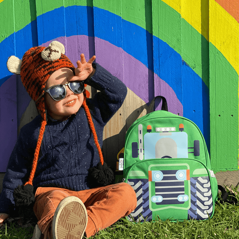 Boy sitting in front of a rainbow next to a green tractor kids backpack.