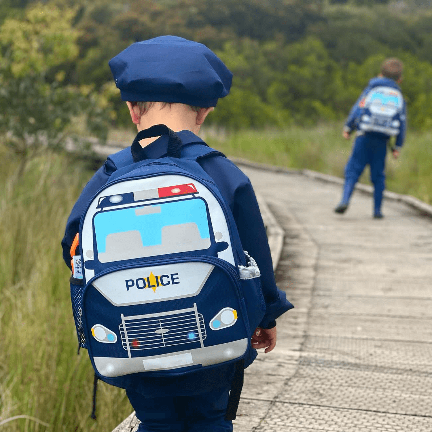 Boy wearing a kids police car backpack on a boardwalk in the forest